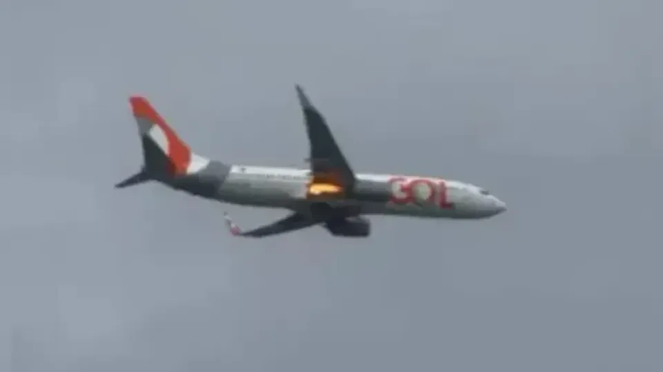 Avião da Gol em voo com chamas visíveis no motor direito, sob céu nublado