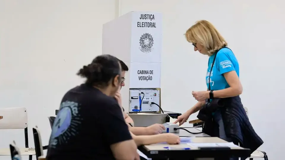 Eleitora se identifica com mesários ao lado da cabine de votação