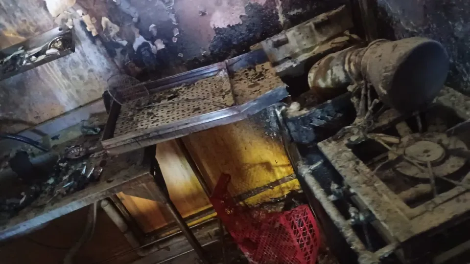 Interior de loja de salgados destruído pelo fogo, com equipamentos queimados e fuligem nas paredes