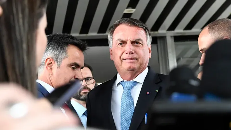 Jair Bolsonaro, de terno escuro e gravata azul, diante de microfones de emissoras