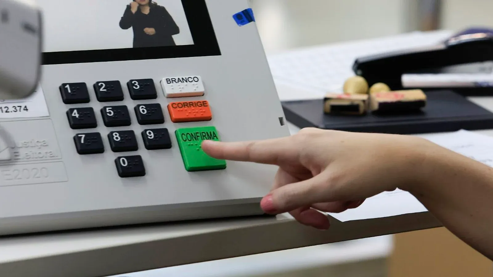 Dedo de eleitor prestes a apertar a tecla verde Confirma de uma urna eletrônica